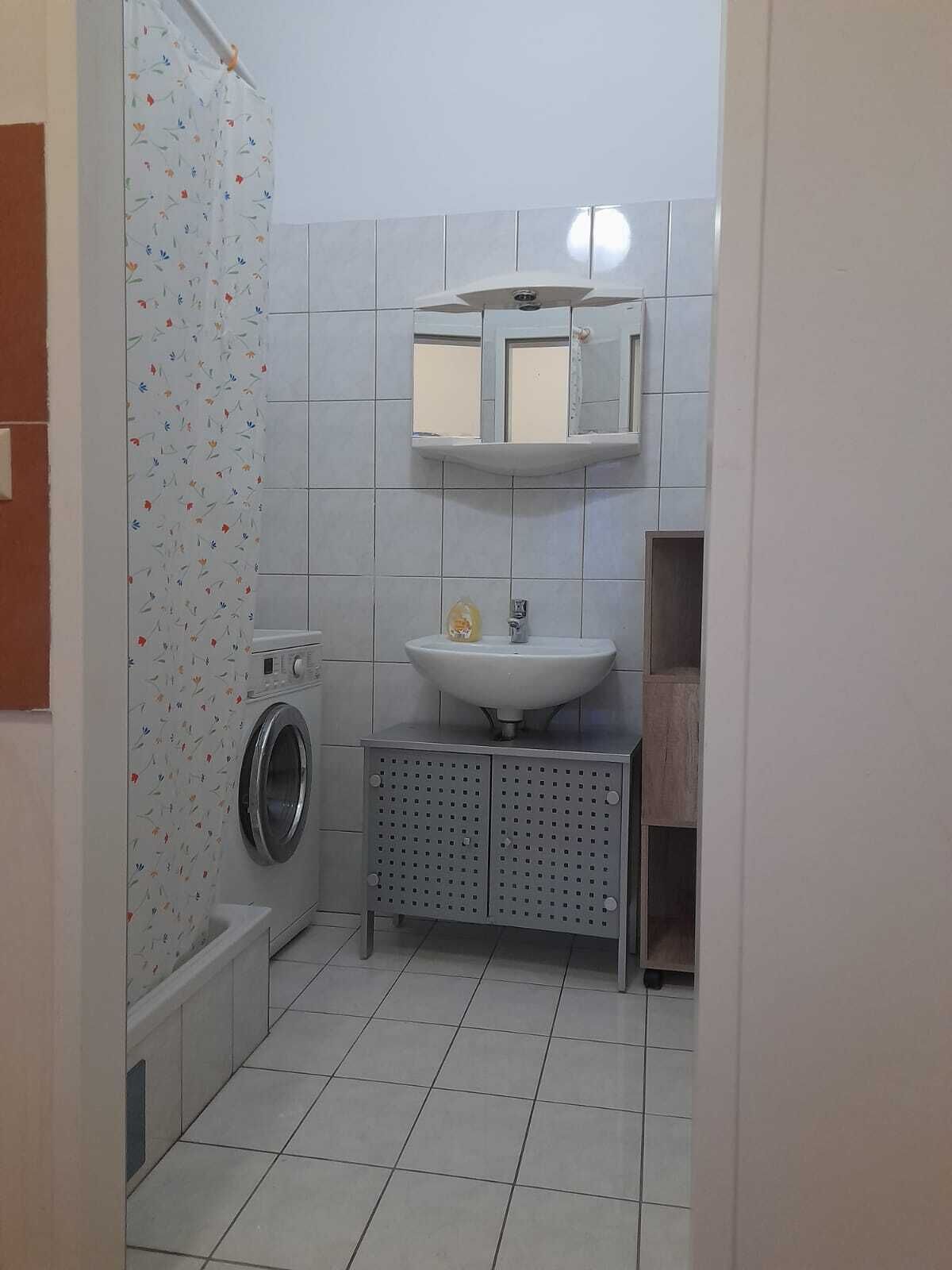 A compact bathroom with a washing machine, a sink, and a mirror above it.