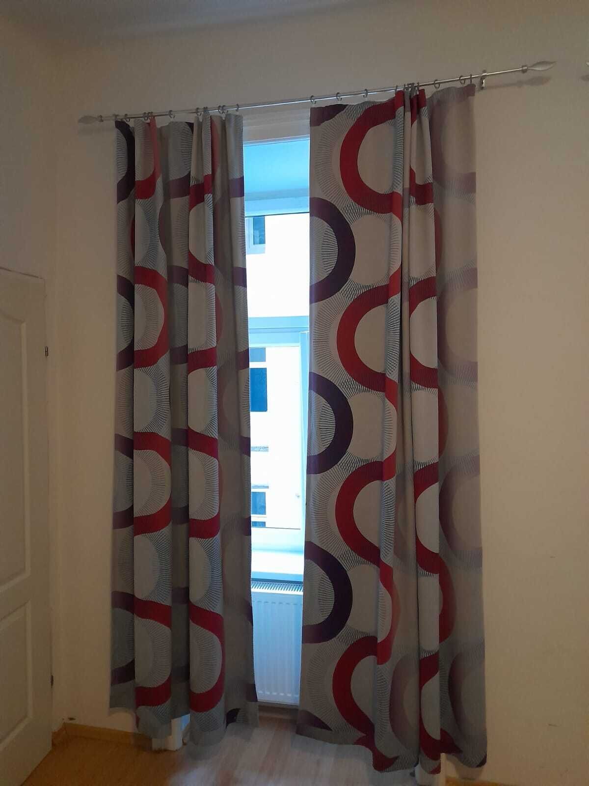 Ein Zimmer mit Tür, einem Fenster mit Blick auf ein Gebäude und einem Vorhang mit geometrischem Muster.