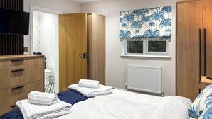 A bedroom with a bed, wooden wardrobe, a bathroom with a toilet, and a window with a blue floral curtain. - 3 bedroom accommodation in Brereton, Cannock Chase (Brereton, Cannock Chase)