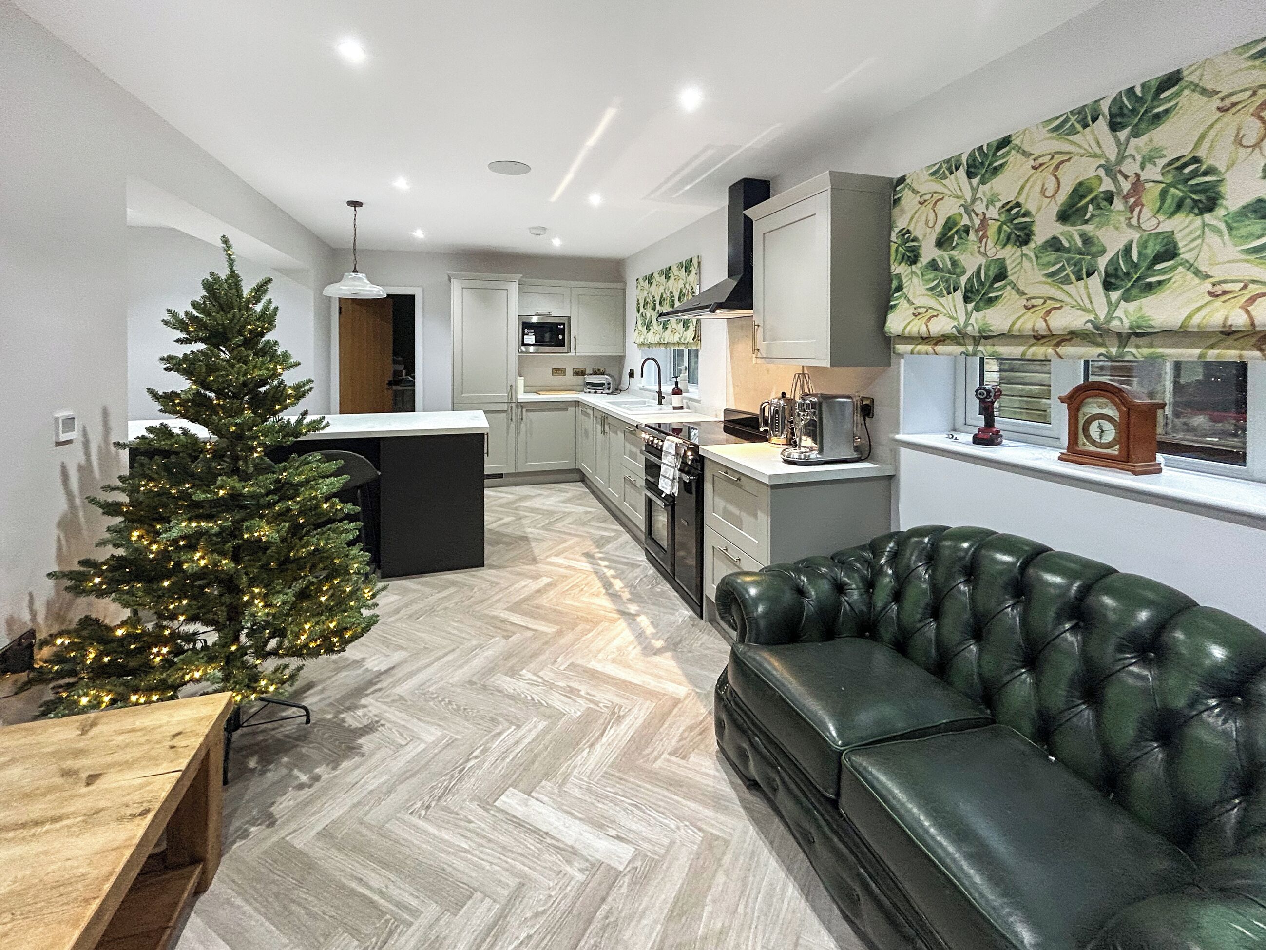 Una cocina moderna con suelo de espiga, un sofá de cuero verde y un árbol de Navidad.