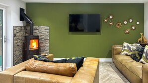 Sala de estar com lareira de pedra, televisão de tela plana e parede verde com espelhos decorativos.