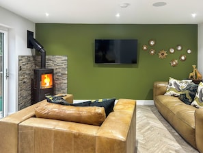 Un salon doté d’une cheminée en pierre, d’un téléviseur à écran plat et d’un mur vert agrémenté de miroirs décoratifs.