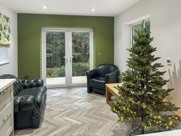 Una sala de estar moderna con una pared verde, un sofá de cuero, un sillón negro, una mesa de centro de madera y un árbol de Navidad decorado.