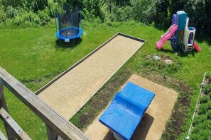 Une aire de jeux avec un trampoline, un toboggan et un espace sablonneux.