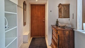 Ein Flur mit einer Holztür, einem weißen Regalelement, einer Holzkommode mit Schubladen und einem Spiegel an der Wand.