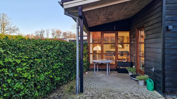 Ein Holzhaus mit überdachter Terrasse, Esstisch und Topfpflanzen.