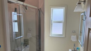 Et moderne badeværelse med en glasafskærmet brusebad, toilet og et spejl med vask.