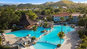 A resort with multiple swimming pools, palm trees, and a mountainous backdrop. - Confresi Palm Beach & Spa (Puerto Plata)