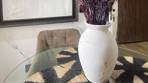 Un interno moderno con un grande dipinto astratto, un vaso bianco con fiori viola e un tavolo in vetro con sottotavolo geometrico.