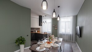 A dining area with a long table set for a meal, a kitchen in the background, and a TV mounted on the wall. - Luxury apart with a view Victory Square (Minsk)