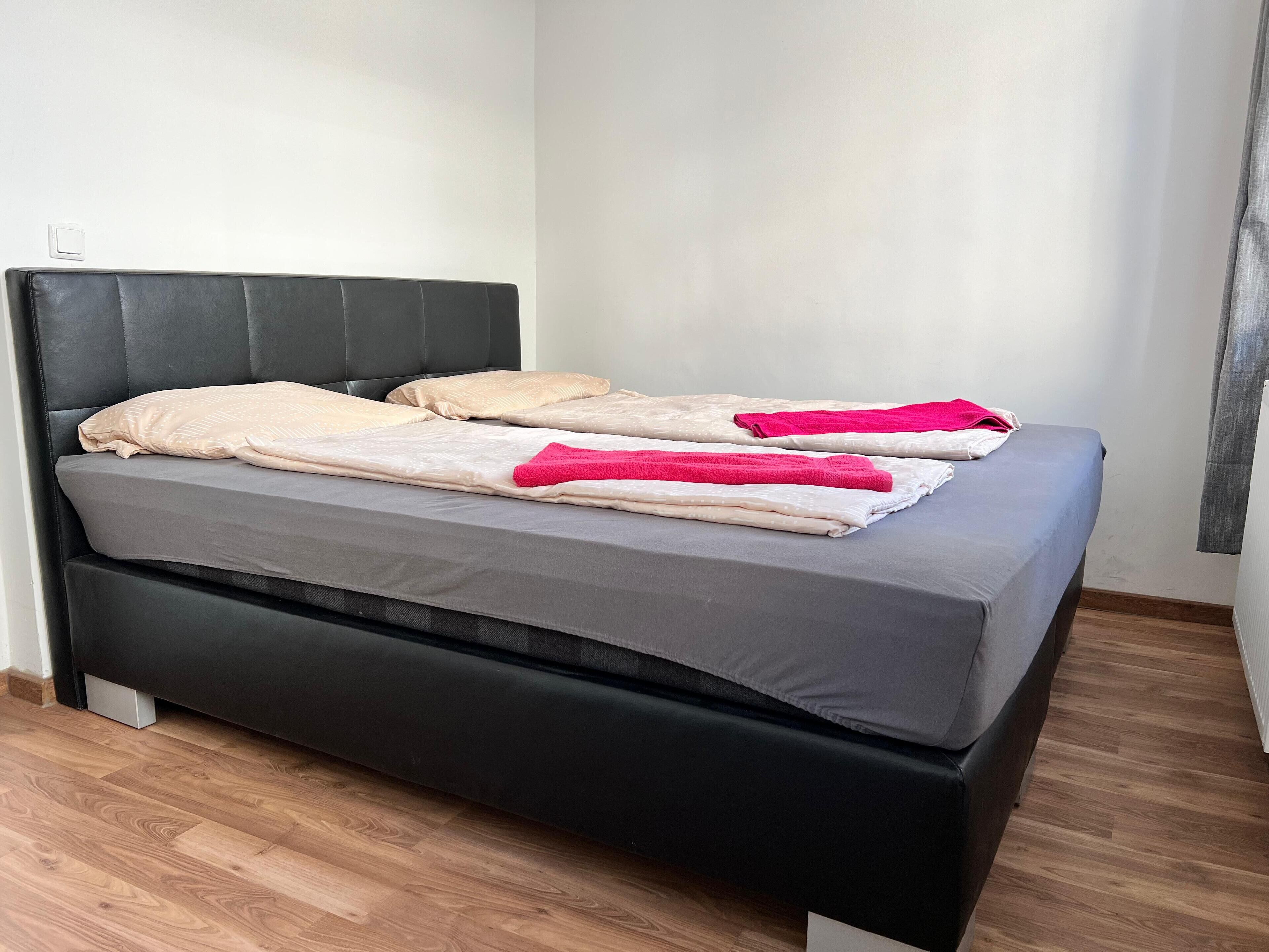 A modern bed with a black headboard, grey bedding, and two pink towels.