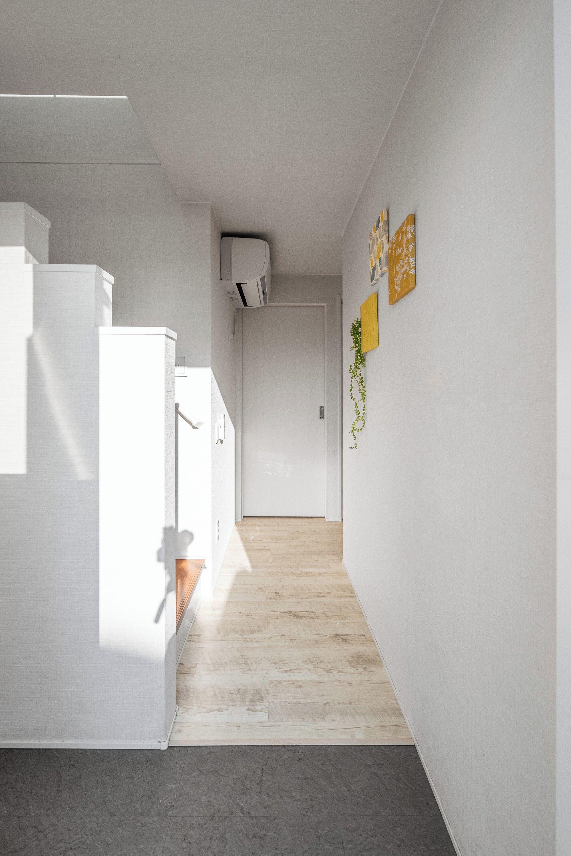 A narrow hallway with a wooden floor, white walls, and a white door at the end.
