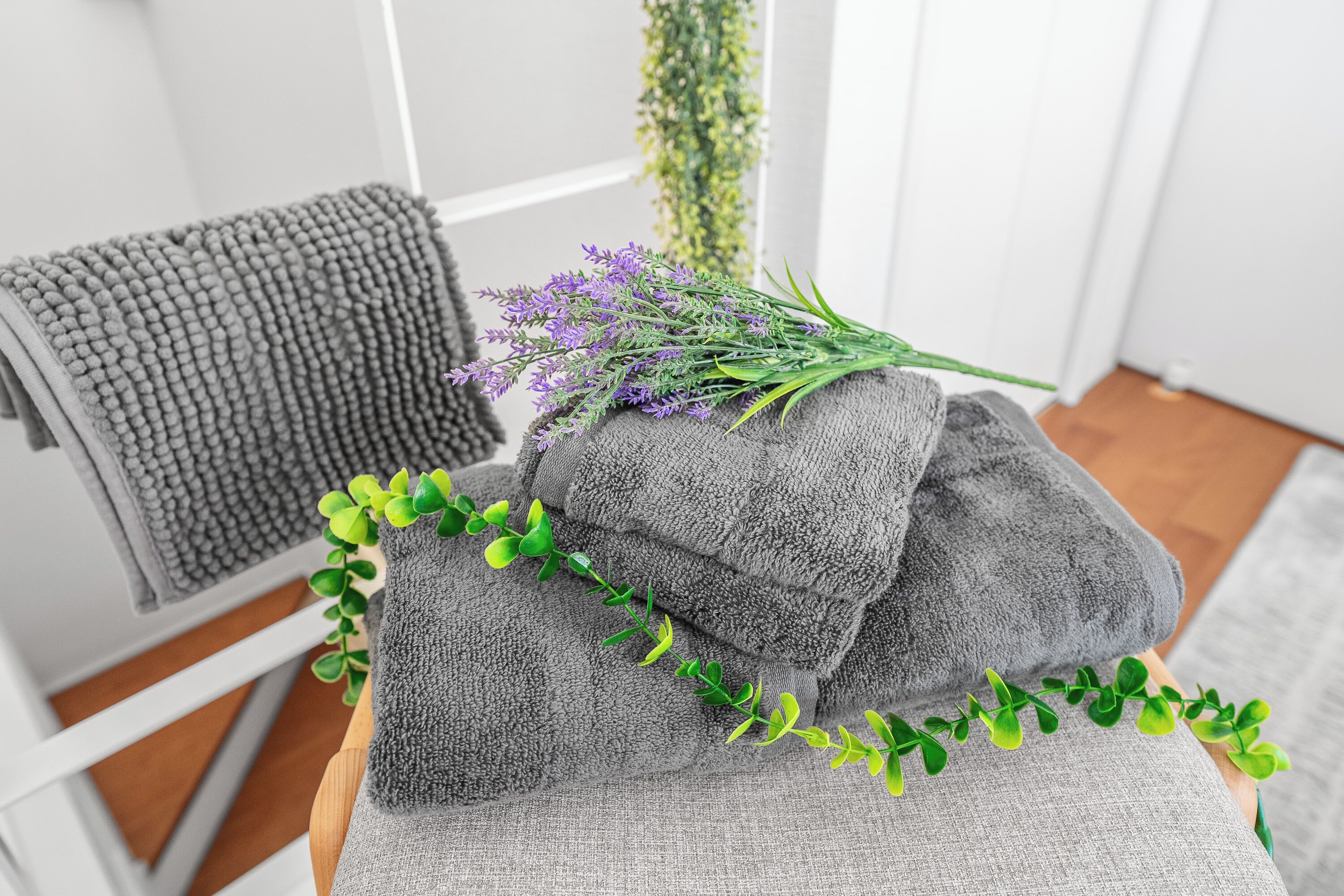 A stack of grey towels with a sprig of lavender and green foliage on a wooden surface.