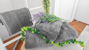 A stack of grey towels with a sprig of lavender and green foliage on a wooden surface.
