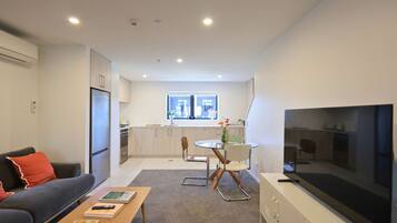 Een modern appartement met een woonkamer, eetgedeelte, keuken en een grote televisie.
