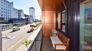 A balcony with a view of a city street, a bench, and a building with a sign. - Newly Built 1BR Apartment near Te Kaha Stadium (Christchurch)