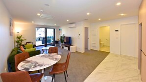 A modern living room with a dining area, a flat-screen TV, and a large window. - Newly Built 1BR Apartment near Te Kaha Stadium (Christchurch)