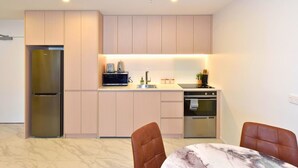 A modern kitchen with a built-in refrigerator, microwave, and oven, a dining area with a marble table and chairs, and light-colored cabinetry. - Newly Built 1BR Apartment near Te Kaha Stadium (Christchurch)