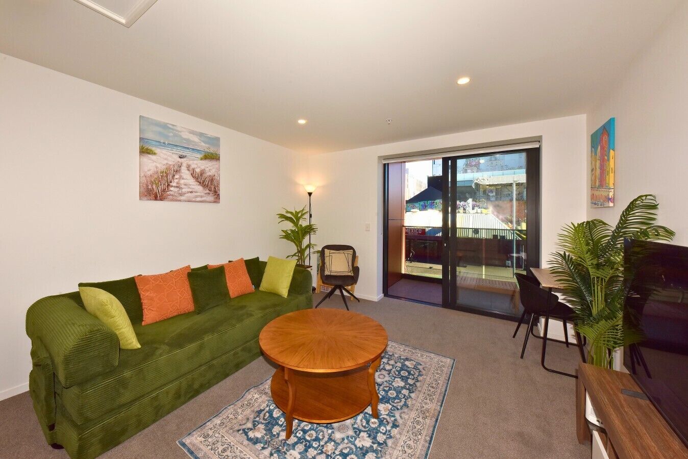 Una sala de estar con un sofá verde, una mesa de centro redonda de madera, un ventanal y vistas a la calle.