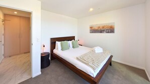 Een slaapkamer met een houten bed, een nachtkastje, een aan de muur hangend schilderij en een deur die naar een andere kamer leidt.
