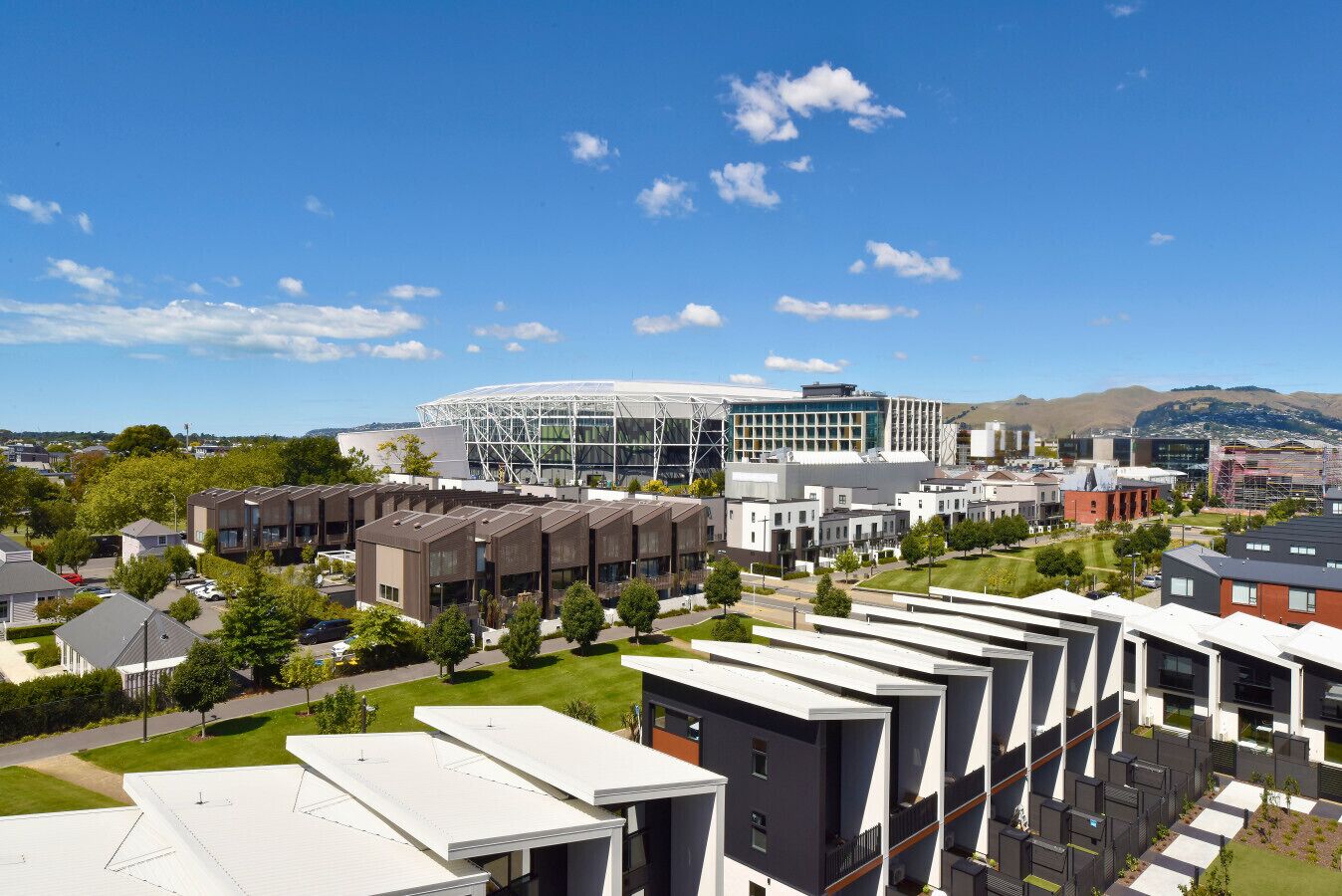 A modern building complex with multiple residential units, a large glass structure, and surrounding greenery.