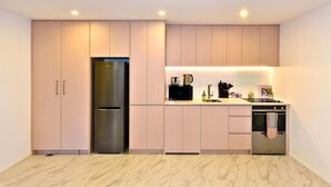 A modern kitchen with light wood cabinets, a stainless steel refrigerator, a coffee maker, and a built-in oven. - Central 1BR Apartment Steps From Te Kaha Stadium (Christchurch)