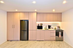Una cocina moderna con armarios de madera clara, un refrigerador de acero inoxidable, una cafetera y un horno empotrado.