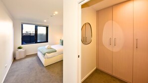A bedroom with a bed, a window, a small plant, and a wardrobe. - Central 1BR Apartment Steps From Te Kaha Stadium (Christchurch)