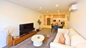 A modern living room with a flat-screen TV, a coffee table, a sofa, and a dining area with chairs. - Central 1BR Apartment Steps From Te Kaha Stadium (Christchurch)
