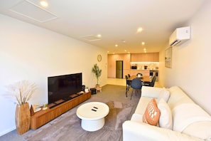 Una sala de estar moderna con un televisor de pantalla plana, una mesa de centro, un sofá y un comedor con sillas.
