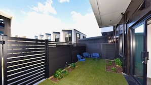 A modern outdoor space with artificial grass, a black fence, and blue chairs. - Central 1BR Apartment Steps From Te Kaha Stadium (Christchurch)