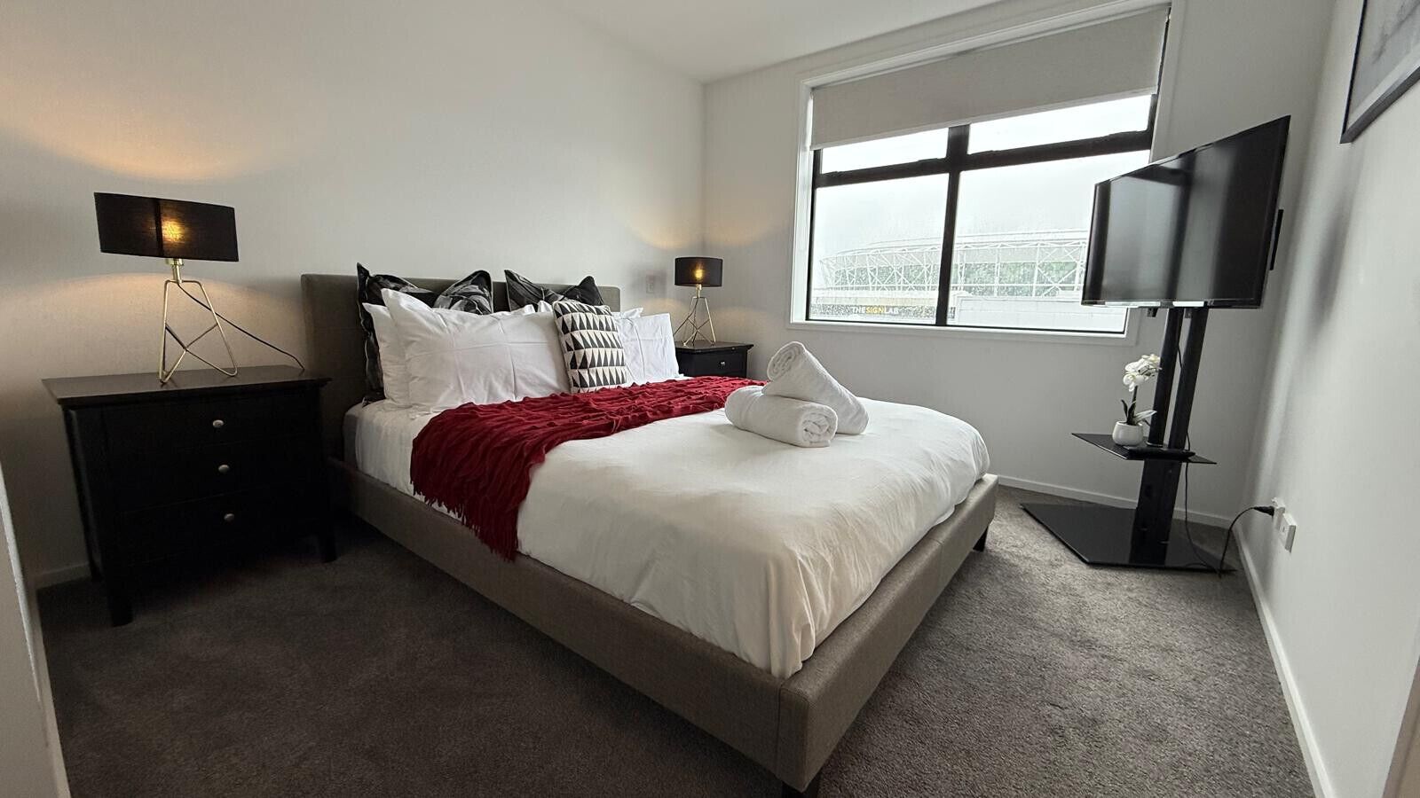 Een keurig opgemaakt slaapkamer met een bed, nachtkastjes, een televisie en een raam met uitzicht.