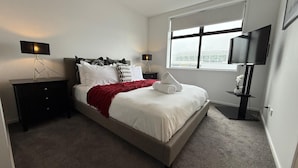 A neatly arranged bedroom with a bed, nightstands, a TV, and a window with a view. - Stylish Cashel Townhouse Stay (Christchurch)