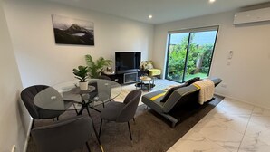A modern living room with a glass dining table, grey sofas, and a flat-screen TV. - Stylish Cashel Townhouse Stay (Christchurch)
