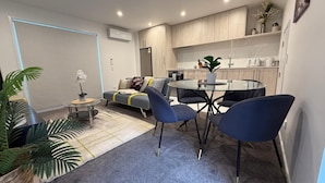 A modern living room with a sofa, a dining table with chairs, a small round table with a chair, and a potted plant. - Stylish Cashel Townhouse Stay (Christchurch)