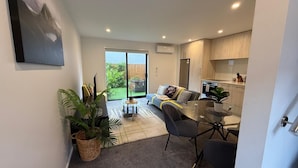 A modern apartment with a living area, kitchen, and a sliding glass door leading to a balcony. - Stylish Cashel Townhouse Stay (Christchurch)