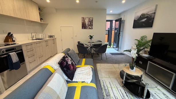 A modern living room with a sofa, a TV, and a dining area. - Stylish Cashel Townhouse Stay (Christchurch)