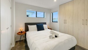 Un dormitorio moderno con una cama grande, un armario y una mesita de noche con lámpara.