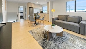 Una sala de estar moderna con un sofá gris, una mesa de centro redonda y un comedor con sillas y una mesa.