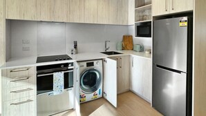 A compact kitchen with a built-in washer and dryer, a stainless steel refrigerator, and wooden cabinetry. - Chic 1-Bedroom Apartment with Balcony in Ferry Rd (Christchurch)