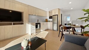 A modern kitchen with built-in appliances, a dining area with a table and chairs, and a flat-screen TV mounted on the wall. - Chic 1-Bedroom Apartment with Balcony in Ferry Rd (Christchurch)