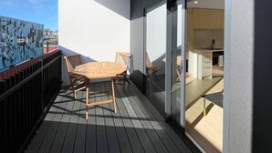 A balcony with a wooden table and chairs, a glass door leading to a kitchen, and a black metal fence. - Chic 1-Bedroom Apartment with Balcony in Ferry Rd (Christchurch)