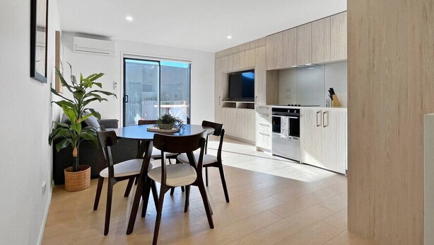 A modern kitchen with white cabinets, a dining area with a table and chairs, and a large window. - Chic 1-Bedroom Apartment with Balcony in Ferry Rd (Christchurch)