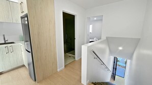 A modern kitchen with a built-in refrigerator, a wooden accent wall, and a staircase leading to a balcony with a view. - Chic 1-Bedroom Apartment with Balcony in Ferry Rd (Christchurch)