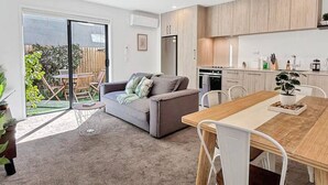 A modern apartment with a dining area, kitchen, and a sliding glass door leading to a balcony with outdoor furniture. - Stylish 2-Bedroom Home with Back Yard (Christchurch)