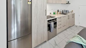 A modern kitchen with a stainless steel refrigerator, wooden cabinets, a countertop with a sink, and a built-in oven. - Stylish 2-Bedroom Home with Back Yard (Christchurch)