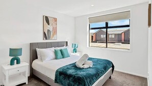 A modern bedroom with a large bed, a nightstand, a window with a view, and a painting on the wall. - Stylish 2-Bedroom Home with Back Yard (Christchurch)