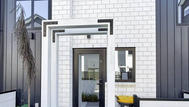 A modern building with a white brick facade, a black-framed entrance, and a small garden area with plants. - Stylish 2-Bedroom Home with Back Yard (Christchurch)