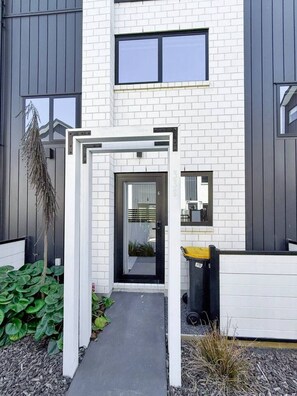 Ein modernes Gebäude mit weiß verputzter Fassade, einem schwarzen Eingangsbereich und einem kleinen Garten mit Pflanzen.