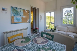 Une pièce comprenant une table, des chaises, un canapé, une fenêtre décorée d’un motif représentant un arbre, et un tableau d’affichage où sont accrochées des cartes et des notes.
